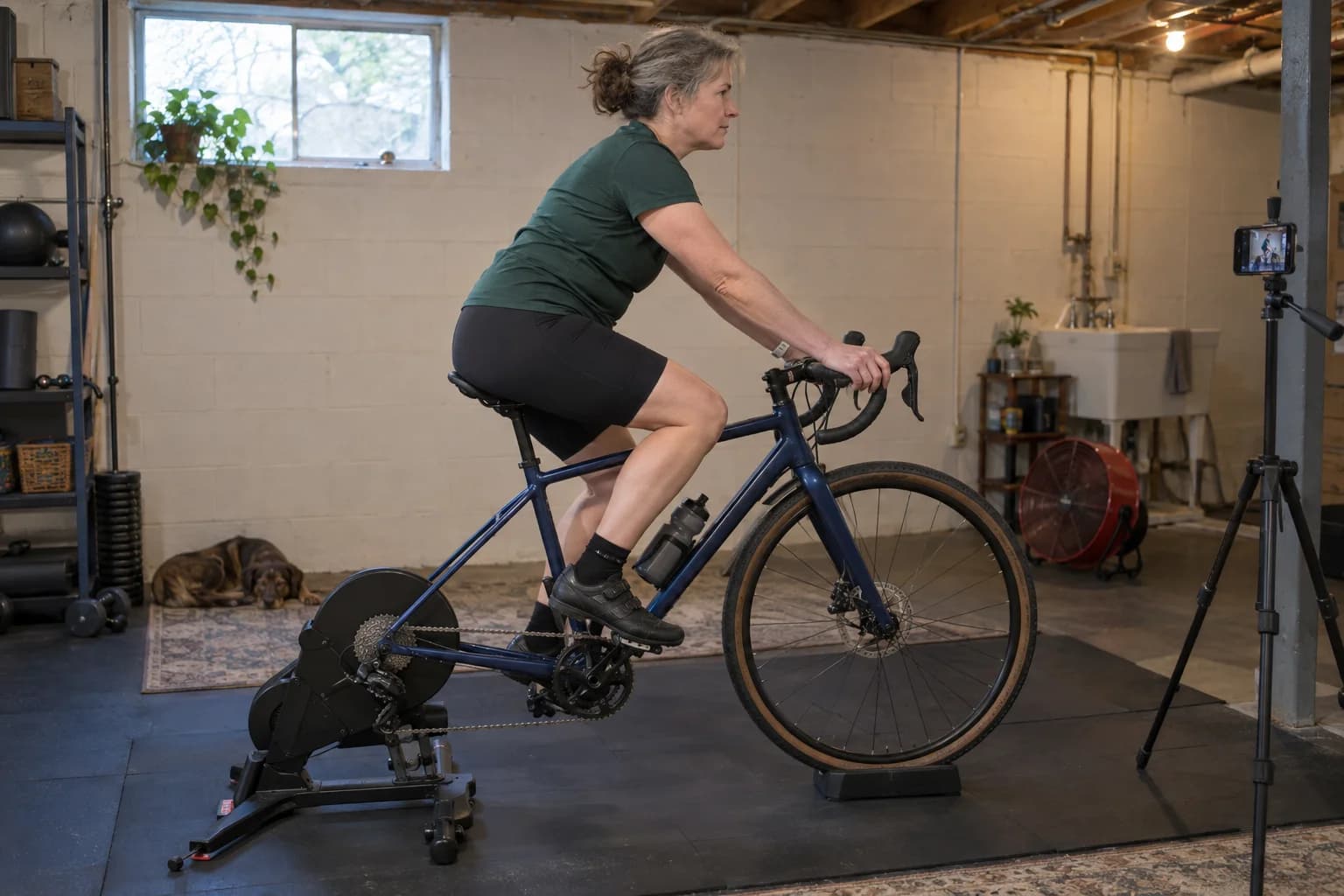 A road rider recording a supported indoor trainer setup with a phone.