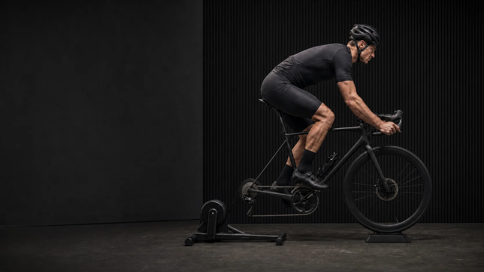 A side view of a cyclist riding on an indoor bike stand.